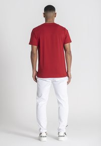 Röd bomullströja, rundad halsringning, korta ärmar, bärs med vita denimbyxor och vita sneakers med svarta textaccenter på klackarna.