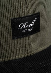 Samtmütze in olivgrün mit einem schwarzen flachen Schirm. Sie verfügt über ein rechteckiges schwarzes Etikett mit weißem, geschwungenem Text und Gründungsjahr.