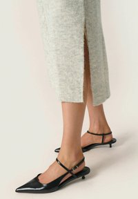 Scarpe slingback nere in pelle con punta affilata, dotate di una sottile cinghia alla caviglia e tacco a kitten, abbinate a un maglione grigio chiaro in maglia con fessure laterali.