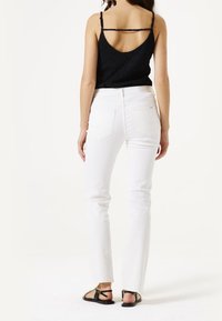 Bílé rovné džíny vyrobené z denimové tkaniny, sladěné s černým texturovaným topem bez rukávů s tenkými ramínky. Sandály s černými popruhy a detailem na přezku.