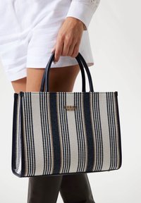 Borsa a tracolla a righe nei colori blu navy, bianco e beige; realizzata in tessuto con due manici e un accento del logo dorato sul fronte.