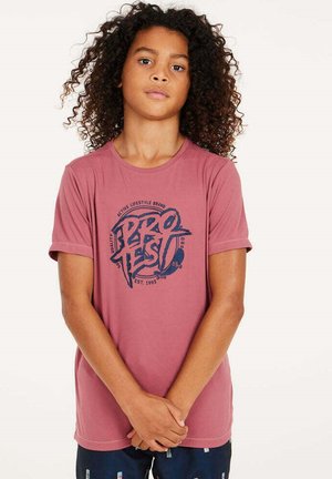 T-shirt rosa a maniche corte con un design grafico blu. Tessuto leggero, colletto rotondo e vestibilità comoda. Il modello è in piedi con le braccia incrociate.