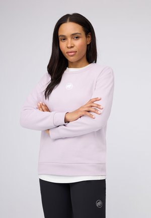 Felpa di colore viola chiaro con scollatura rotonda, polsini e vita a costine; presenta un piccolo logo bianco sul petto. Indossata sopra pantaloni neri.