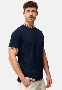 Mørkeblå kortærmet polo med knaplukket henley-krave, der har stribede detaljer på kraven og ærmerne. Blød stoftekstur.
