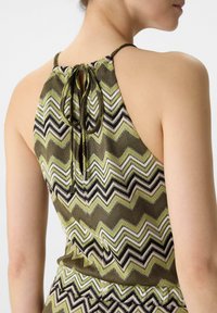 Green and beige patterned halter top with a chevron design. Features a gathered back with a tie closure and textured fabric.