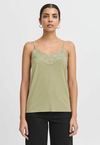 Canotta verde oliva con delicata decorazione in pizzo lungo il collo. Spalline sottili regolabili e una consistenza morbida e liscia. Pantaloni neri.