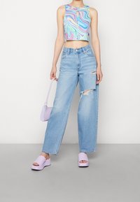 Débardeur multicolore à encolure arrondie, associé à un jean taille haute bleu clair à jambes larges avec des accents déchirés et des sandales à plateforme violettes.