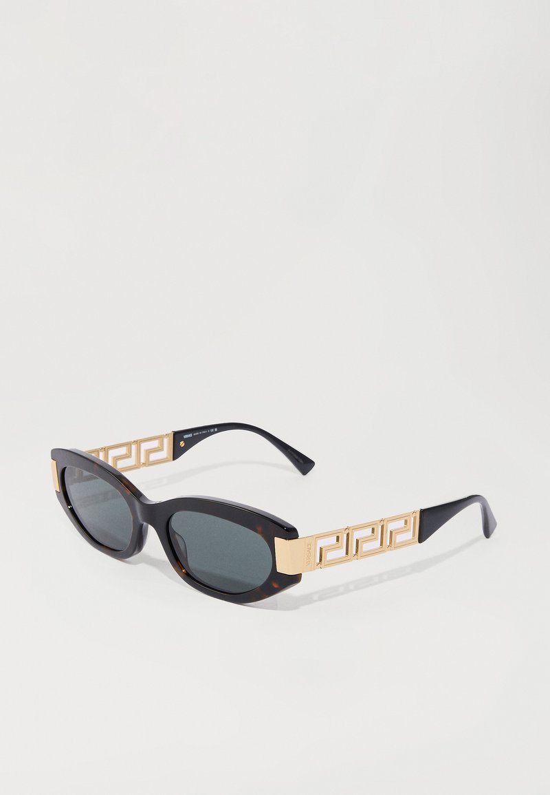 Schwarze Sonnenbrille mit dunklen Gläsern; übergroßes Schildpattgestell mit goldenen geometrischen Akzenten an den Bügeln.