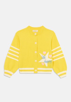Gul strikket cardigan med hvite striper, rund hals og fem knapper. Har broderi av stjerner og hjerter med teksten "Still Happy."