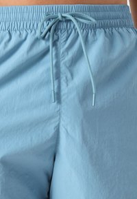 Shorts bleu clair en tissu lisse et léger avec une taille élastique et un cordon de serrage ajustable. Coutures minimales et sans poches.