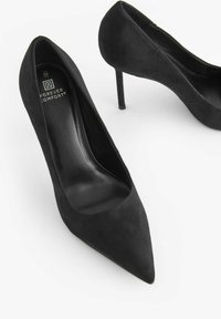 Décolleté in suede nero con tacco alto, dalla punta affusolata e dal profilo elegante. Le solette sono in pelle nera, con un delicato dettaglio del logo.