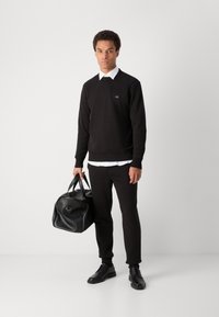 Sweatshirt preto de algodão com decote redondo, usado sobre uma camisa branca de colarinho; combinado com calças de fato pretas e uma elegante bolsa de couro preta.