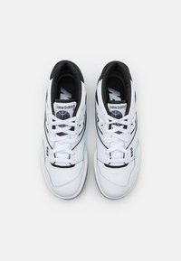 Valkoinen ja musta New Balance 550 -lenkkarit parina nähtynä ylhäältä päin, joissa on valkoiset nauhat ja musta sisävuori valkoista taustaa vasten.