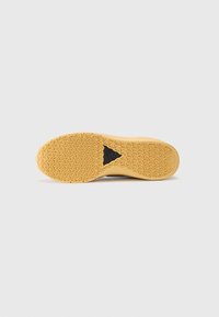 Sola de sapato de borracha em bege com um padrão de aderência texturizado. Apresenta um destaque triangular preto e um contorno curvado para flexibilidade.