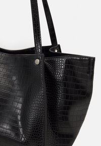 Musta tekonahkainen olkalaukku krokotiilitekstuurilla, jossa on kaksi pitkää kantokahvaa ja metalliset yksityiskohdat sivuilla.