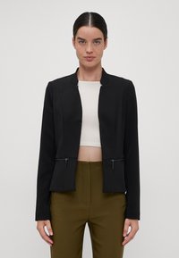 Fekete cropped blézer kerek nyakkivágással, hosszú ujjal és két cipzáros zsebbel elöl. Simább anyag, minimális varrási részletekkel.