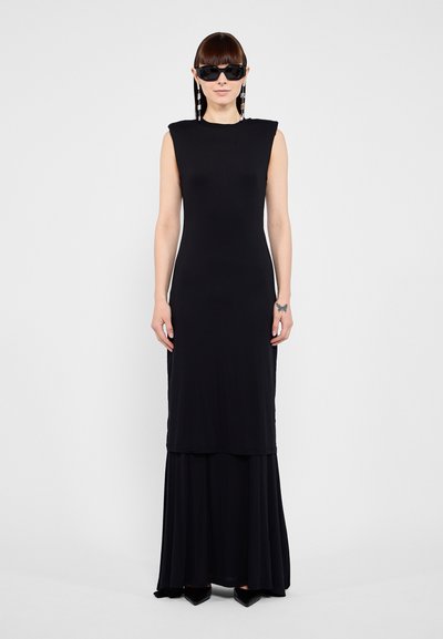 Black sleeveless maxi dress with a layered design, smooth texture, and full-length skirt. Worn with black sunglasses and pointed heels.