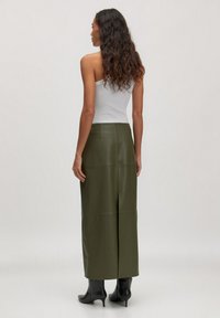 Olijfgroene leren maxi-jurk met een aansluitende taille, met een rechte silhoët en subtiele stiksels. Gecombineerd met zwarte haklaarzen.