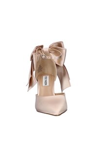 Beige satin high-heel shoe with pointed toe, ankle strap with buckle, and large decorative bow on the heel.