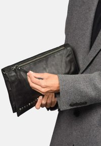 Clutch de cuero negro con cierre de cremallera, adornado con tachuelas plateadas en el borde. Tiene una textura suave y una forma rectangular.