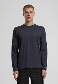 Långärmad, mörkgrå T-shirt gjord av slät bomull med rund halsringning och rak fåll, bärs med svarta byxor. Inga synliga mönster eller detaljer.