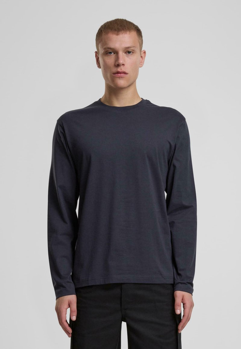 Långärmad, mörkgrå T-shirt gjord av slät bomull med rund halsringning och rak fåll, bärs med svarta byxor. Inga synliga mönster eller detaljer.