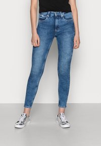Vaqueros skinny de denim desgastado con una cintura alta, que cuentan con cinco bolsillos y un cierre de cremallera. Combinados con zapatillas plateadas.