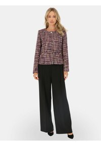 Dopasowana, wielokolorowa marynarka z tweedu z okrągłym dekoltem i zapięciem na guziki, w połączeniu z czarnymi spodniami o wysokim stanie i czarnymi szpilkami.