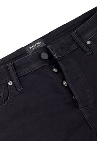 Černé džínové kalhoty s knoflíkovým zapínáním, částečně otevřené, viditelné poutka na pásek, nýty a štítek značky Jack & Jones uvnitř pásku.