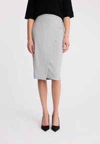 Szara spódnica o kroju kopertowym, z gładką teksturą i długości do kolan, w komplecie z czarnymi szpilkami w szpic.