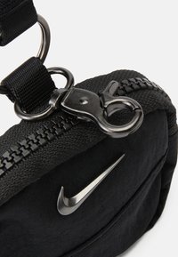 Fekete szövet táska ezüst Nike logóval, cipzáros záródással és kapcsos horgokkal. A dizájn jellemzője a texturált felület és a pánt.