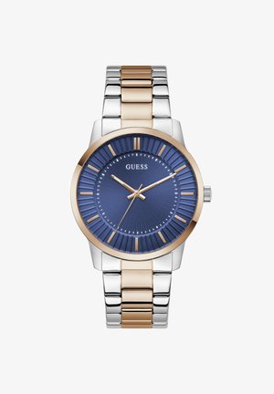 Montre-bracelet pour homme avec cadran texturé bleu, index et aiguilles de couleur or, bracelet métallique bi-tons argent et or, et logo "GUESS" à 12 heures.