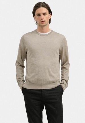Beige sweater i blødt strikmateriale med lange ærmer og rund halsudskæring, parret med sorte bukser. Enkelt, klassisk design, glat tekstur.