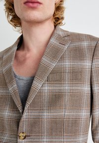 Brown and blue plaid blazer with a notched lapel and single button closure, made of textured fabric. Gray undershirt visible beneath.