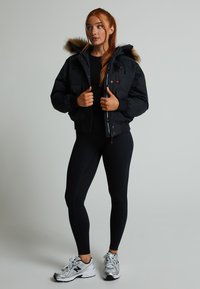 Fekete puffkabát, szőrmebéléses kapucnival, cipzáros elülső résszel és két elülső zsebbel. Fekete topszal viselve, fekete leggingszel és szürke edzőcipővel párosítva.