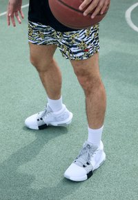 Krepšinio šortai ryškiai tigro raštu su geltona, juoda ir balta spalvomis. Balti sportiniai bateliai su pilkais akcentais ir juodu kulno detalėmis.