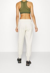 Olijfgroene sportbeha met een racerback ontwerp, gecombineerd met lichtgrijze joggingbroek met een taps toelopende pijp en elastische tailleband.