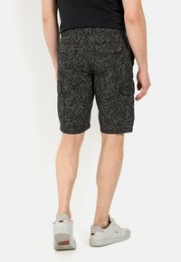 Zwarte cargoshorts met een bladerenpatroon, voorzien vanzijzakken en een aansluitende tailleband, gedragen met witte sportschoenen.