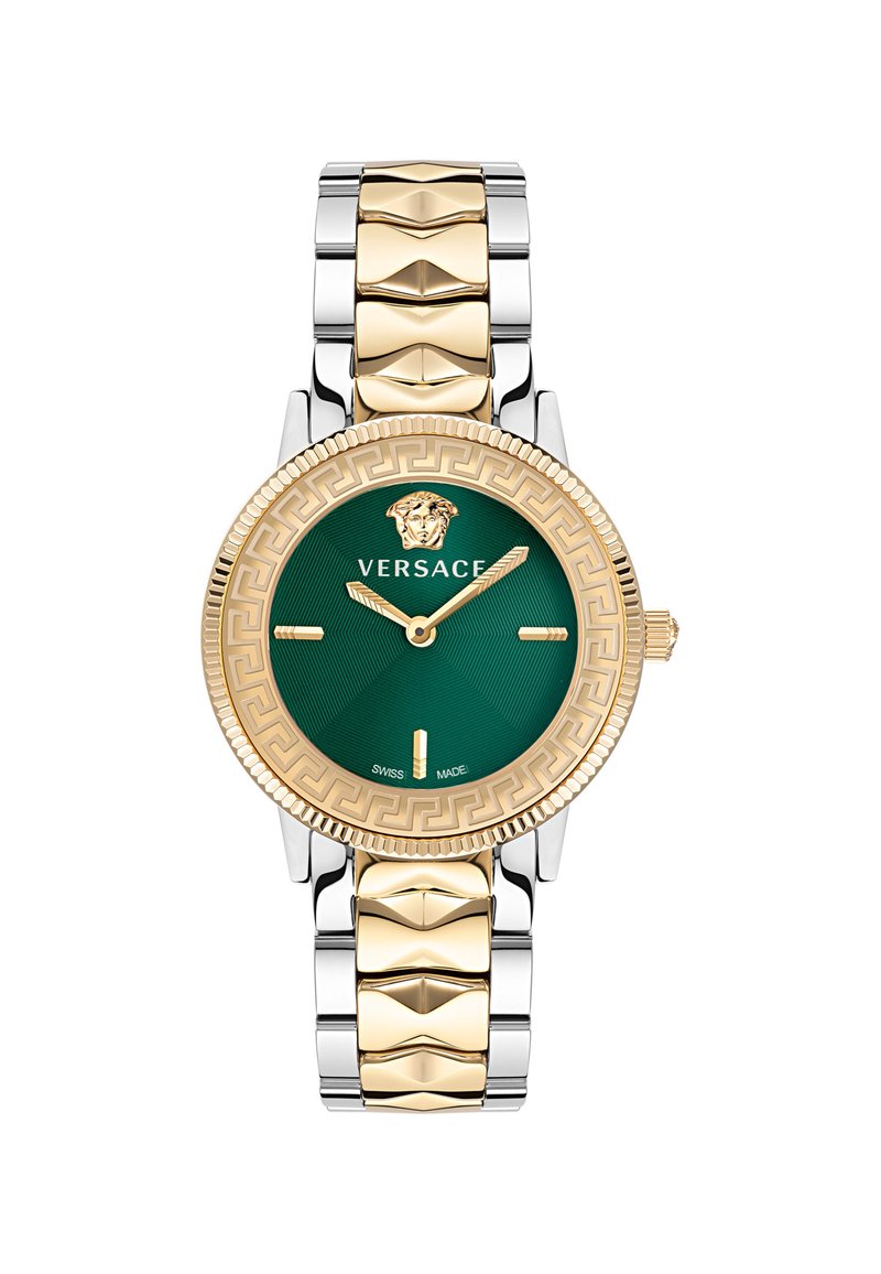 Versace kell, millel on kuldse tooni raami, roheline kellasefär ja hõbedasest lingibraatia. Märkimisväärsed detailid hõlmavad lõvi embleemi ja Kreeka võtmemustrit.