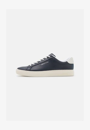 Zapatilla de cuero azul marino con cordones y lengüeta blancos. Cuenta con un talón blanco y suela de goma crema. Nombre de la marca impreso en blanco en el costado.