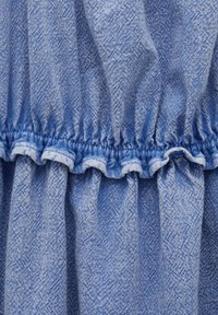 Jasnoniebieska tkanina z teksturowanym wzorem, z marszczonymi falbanami w talii i tonowanym przeszyciem wzdłuż krawędzi.