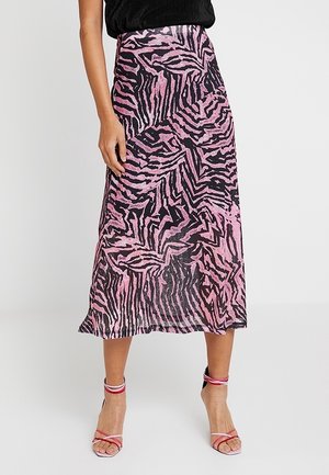 Kvinde iført en midterlang nederdel med pink og sort abstrakt zebraprint kombineret med pink sandaler med høj hæl og stropper.