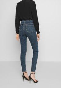 Högmidjade blå jeans med slim fit, tillverkade av denim. Har bakfickor och en uppvikning vid anklarna. Parats med en svart långärmad topp.