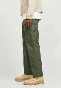 Pantaloni cargo verzi, confecționați dintr-o țesătură ușoară, cu buzunare laterale, design cu picior drept și asortați cu pantofi bej cu șireturi.