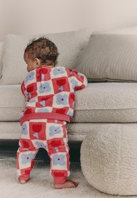 Fleece-pyjamasetti, jossa on punainen, sininen ja kerma väri kukkakuviolla. Paidassa ja housuissa on pehmeä tekstuuri, jossa on kiinteä punainen vyötärö.
