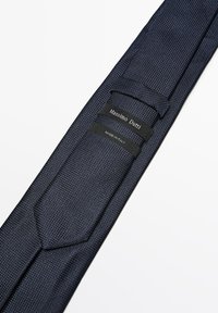 Cravate bleu marine foncée avec un tissage texturé. Les étiquettes incluent "Massimo Dutti" et "Fabriqué en Italie", situées près de l'extrémité étroite de la cravate.