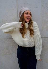 Cream knit sweater with a high, folded neckline and cable knit details, paired with dark jeans and a light-colored beret.