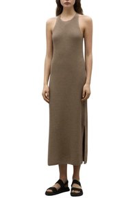 Vestido largo beige con canalé y sin mangas, con una abertura lateral. Presenta una silueta ajustada y una textura lisa, combinado con sandalias planas negras.