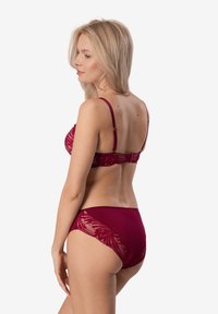 Bordowy zestaw bielizny składający się z koronkowego biustonosza z regulowanymi ramiączkami oraz pasujących majtek o wysokim stanie, zdobionych skomplikowanymi wzorami kwiatowymi.