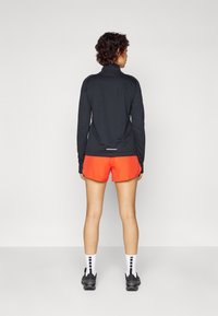 Un haut noir à manches longues associé à un short orange vif, des chaussettes blanches avec des rayures noires, et des chaussures de sport noires. Design simple.